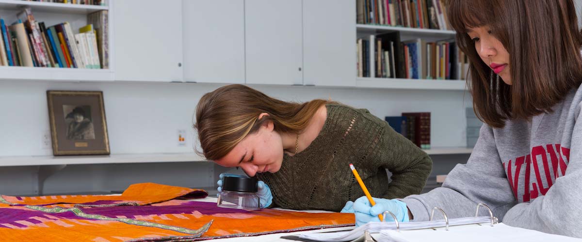 One student looking at fabric while the other takes notes
