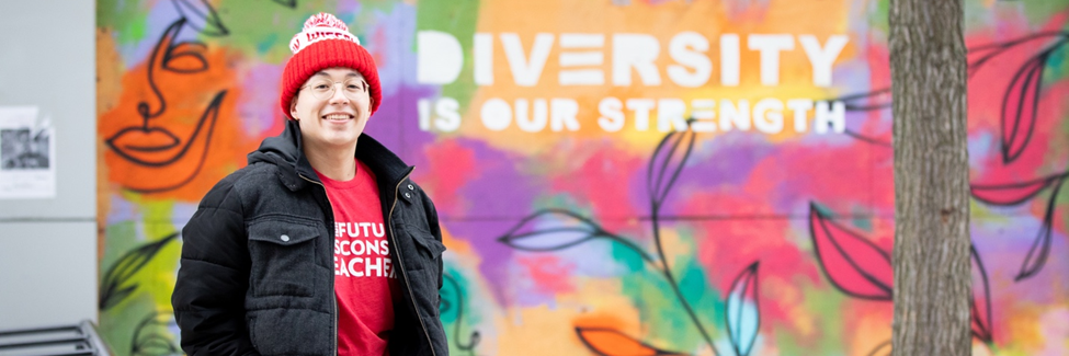 Student poses for a picture. In the background, a mural reads 'Diversity is our strength'