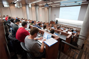Students listen and take notes on their laptop computers during an economics class.