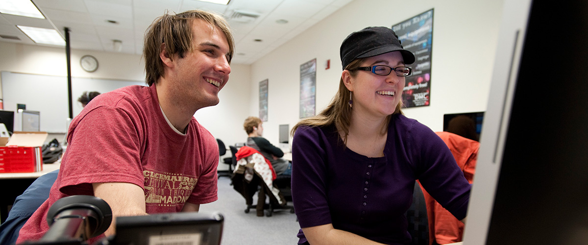 Two students smiling while looking at a computer screen